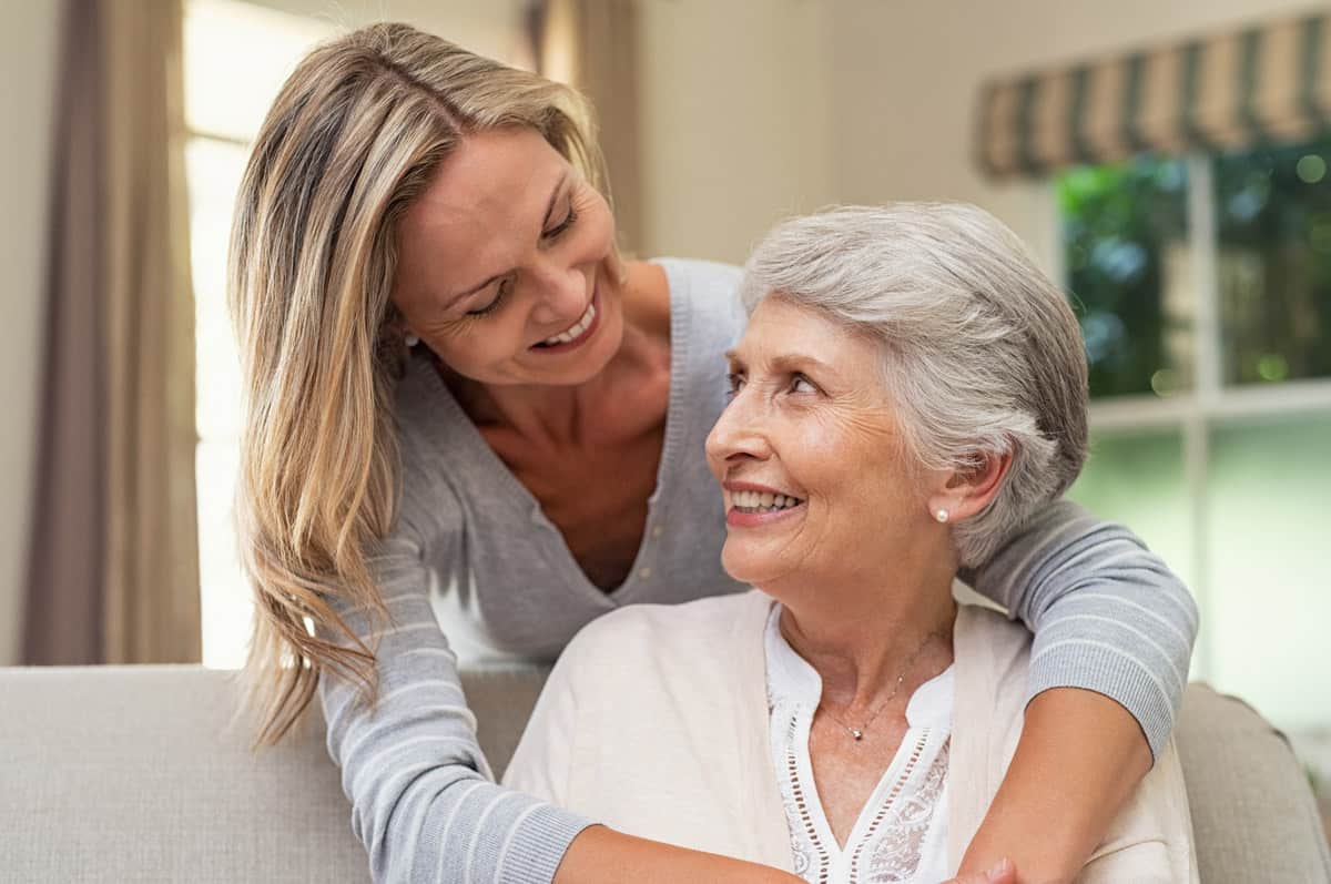 A daughter leans over her mother and they share a smile. Both look comfortable and happy together at Traditions of Grove City in Grove City, OH.