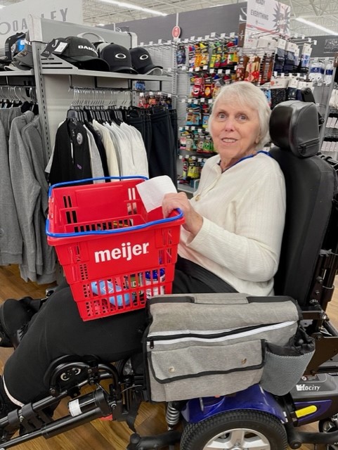 an elderly woman on a motorized wheelchair holding a shopping basket at a Meijer grocery store