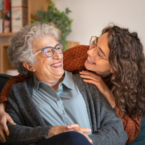 Female senior living resident at Grove City Senior Living getting a hug from her daughter while sitting down on a couch