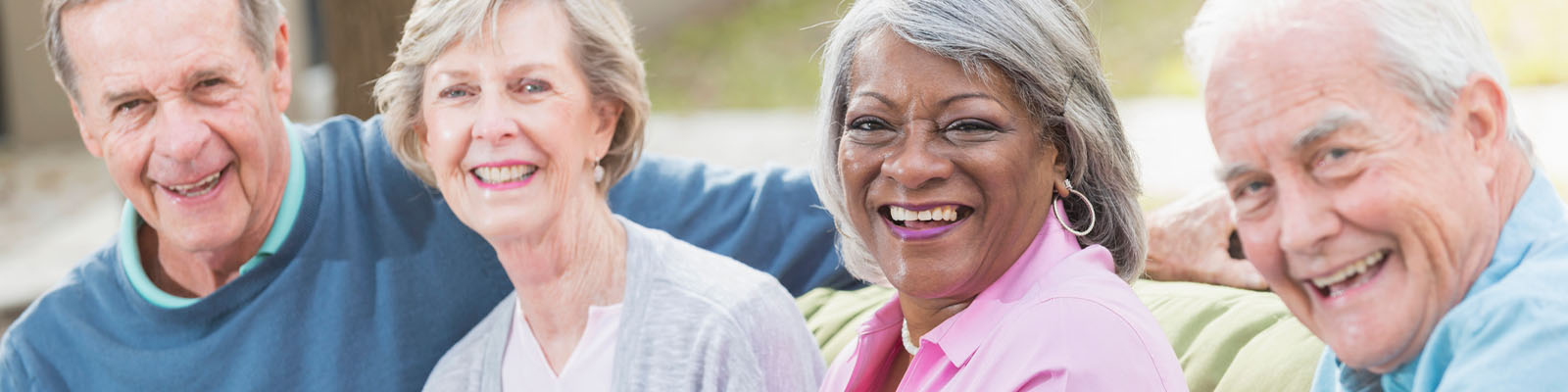 Two male and two female senior living residents with their arms around each other smiling outdoors
