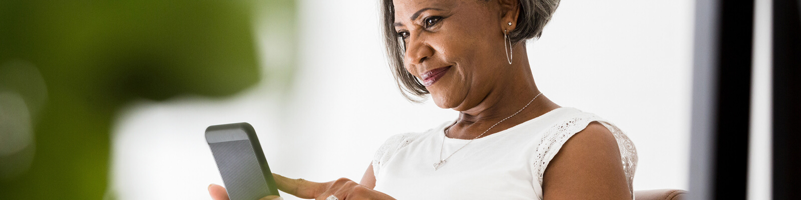 Senior woman wearing a white shirt smiling looking down at smartphone