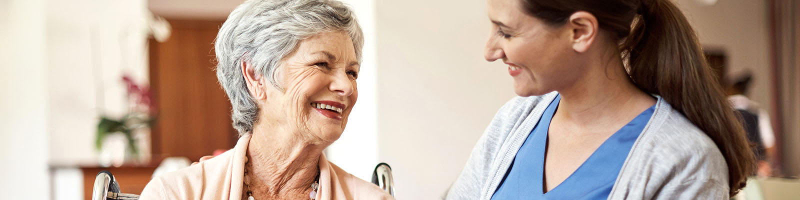 A female senior living resident smiling and looking over at a female nursing assistant