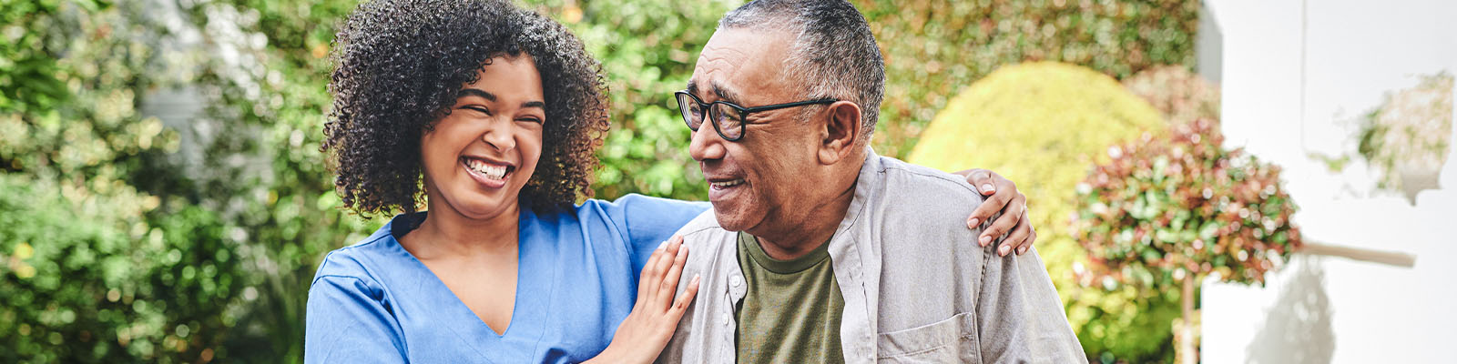 A female nursing assistant smiling and putting her arms around a male senior living memory care resident