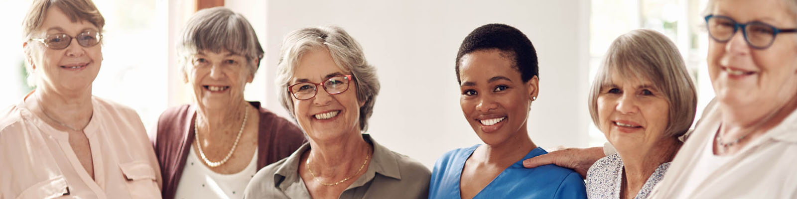 Five senior living residents standing around a female nursing assistant and smiling