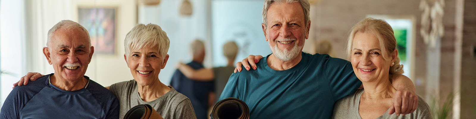 A group of two male and two female senior living residents standing and holding yoga mats while smiling