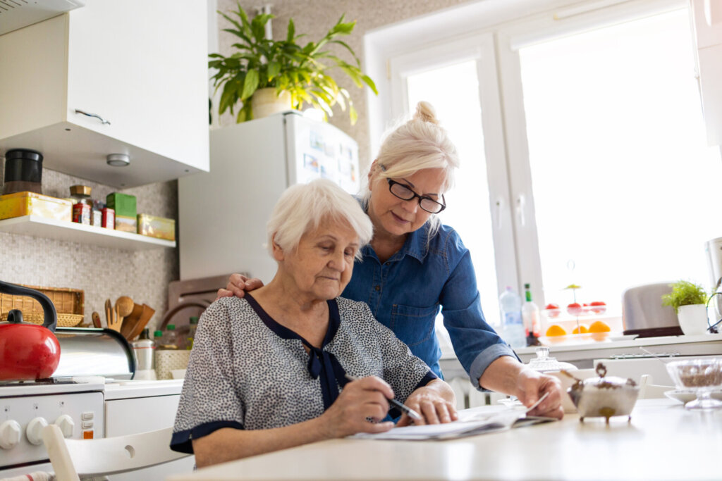 Senior woman sitting at her kitchen table in her independent living apartment doing paperwork with her daughter