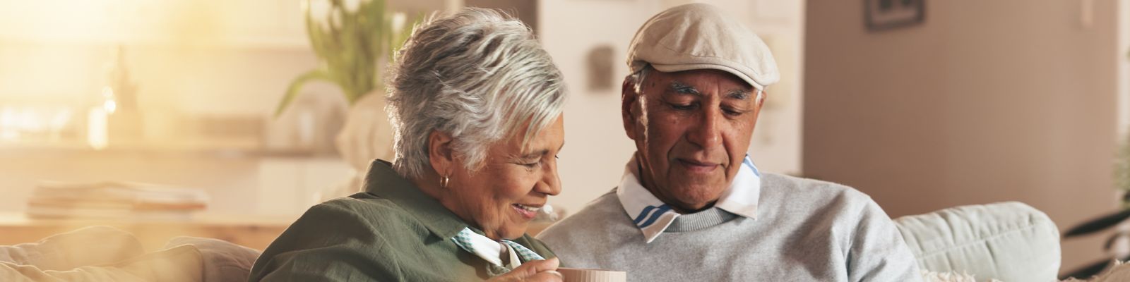 Older couple sitting together on a couch; the man is holding an iPad that he and the woman are looking down at.